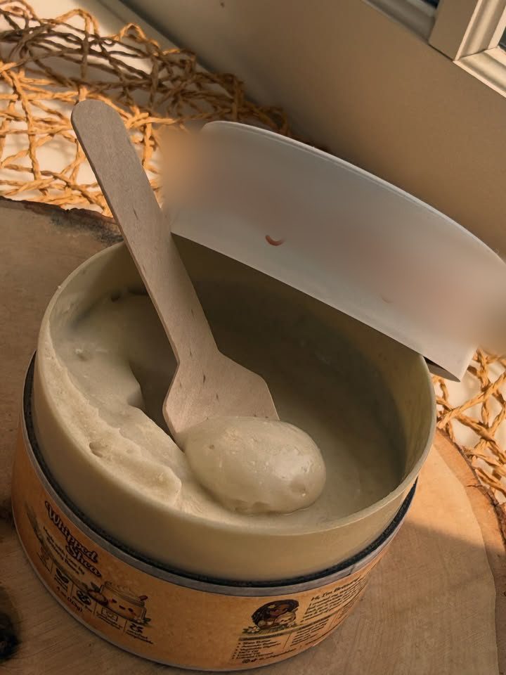 A wooden scoop lifting whipped shea butter out of an open jar