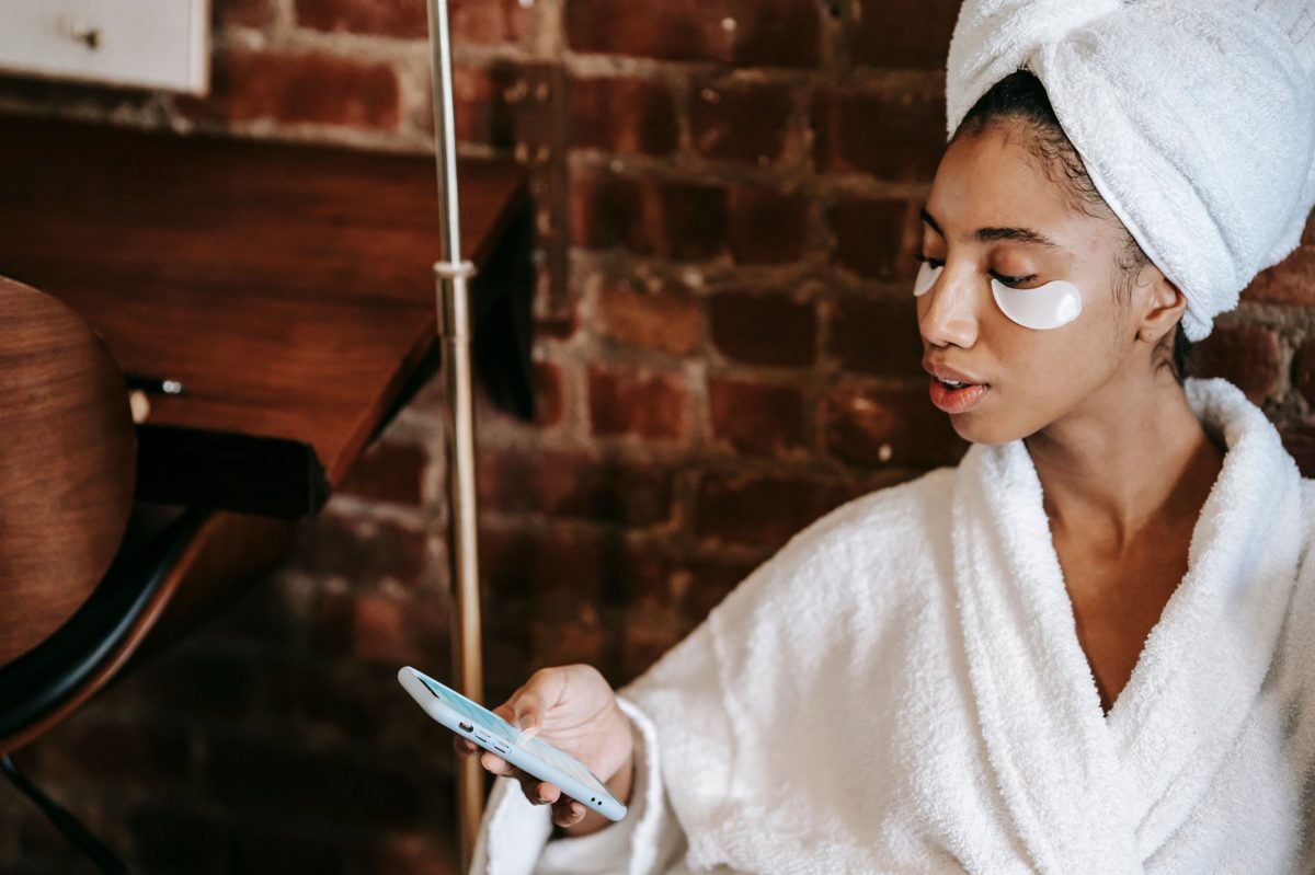 A woman in a white robe and hair towel looking at her phone